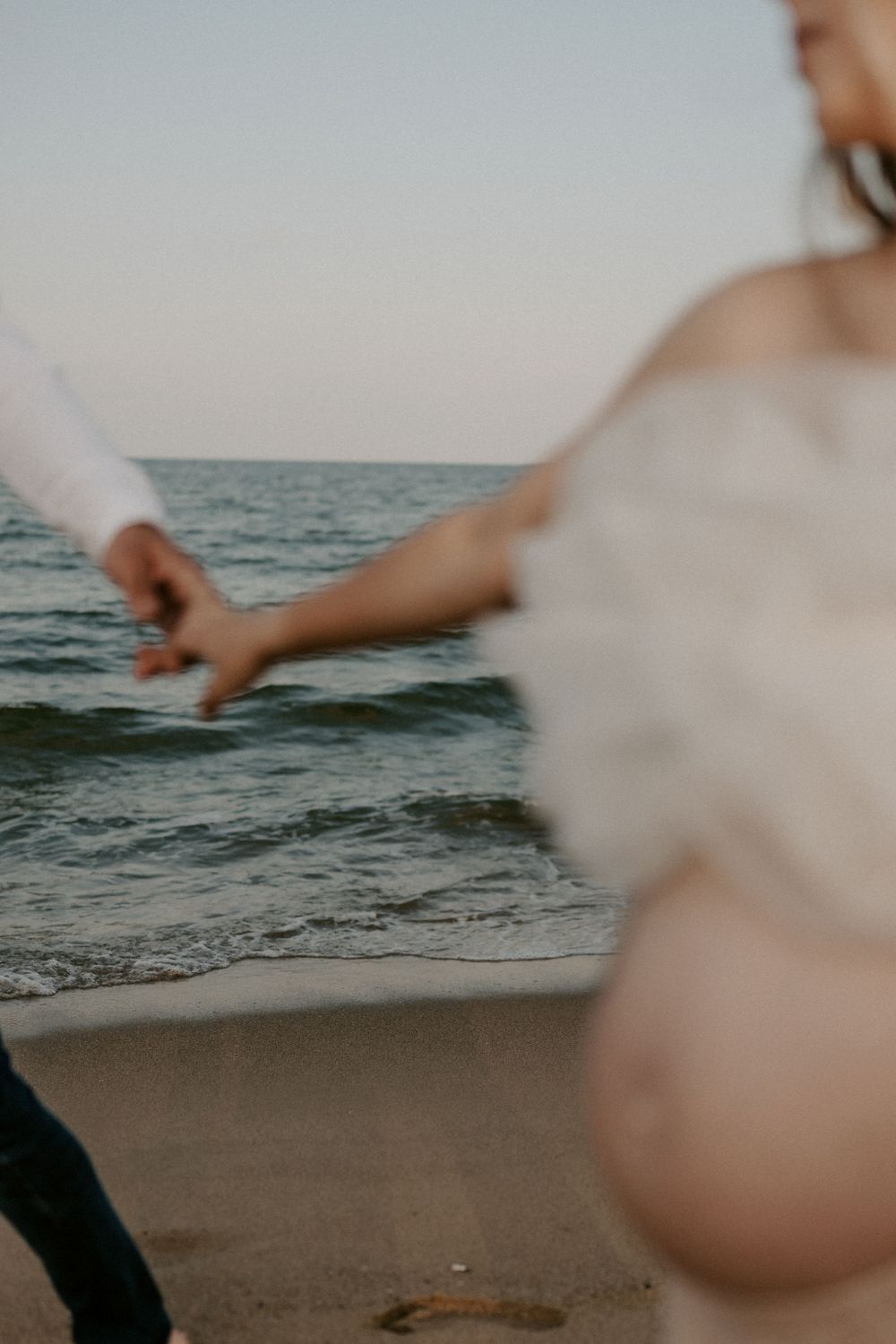 Ocean waves crash onto the sandy shore as figures walk along the beach.