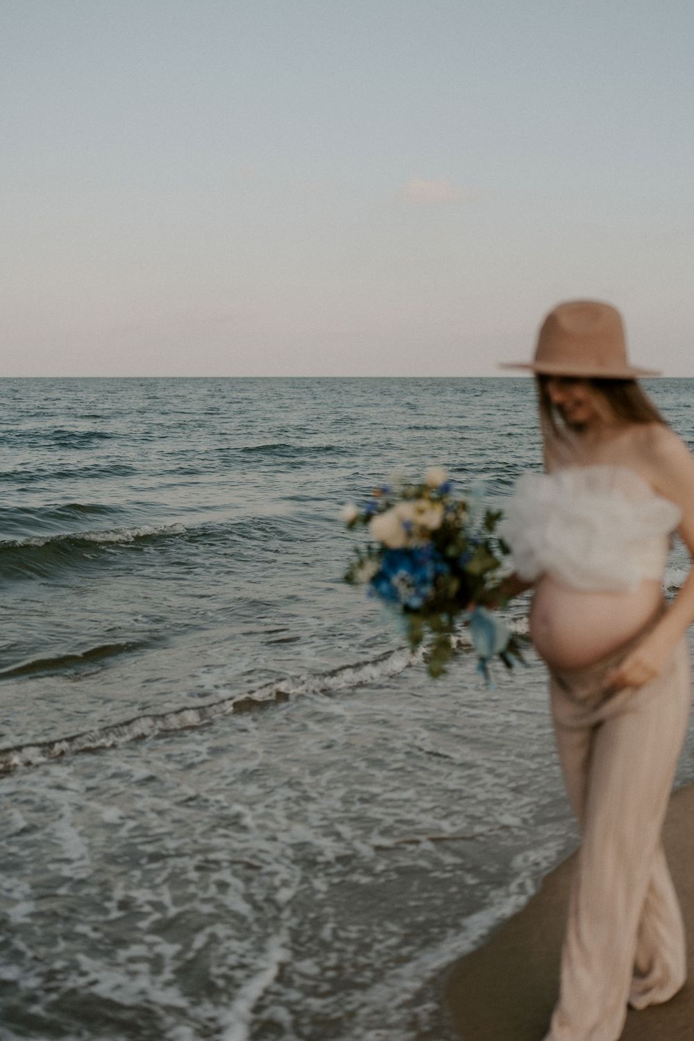 Someone holding a bouquet walks into the ocean waves at sunset.