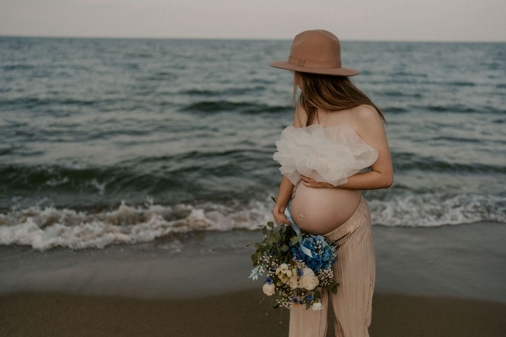 Dreamy beach scene with figure holding flowers against ocean waves.