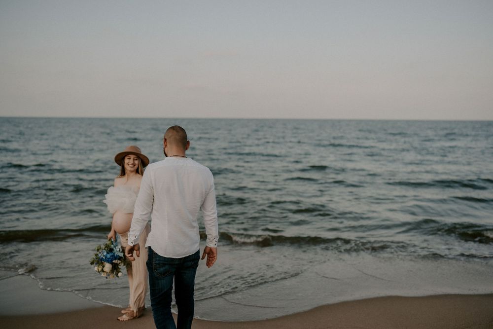 Couple shares intimate moment during beach maternity photoshoot at dusk.