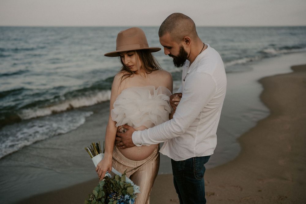 Tender moment between couple during seaside maternity photoshoot.
