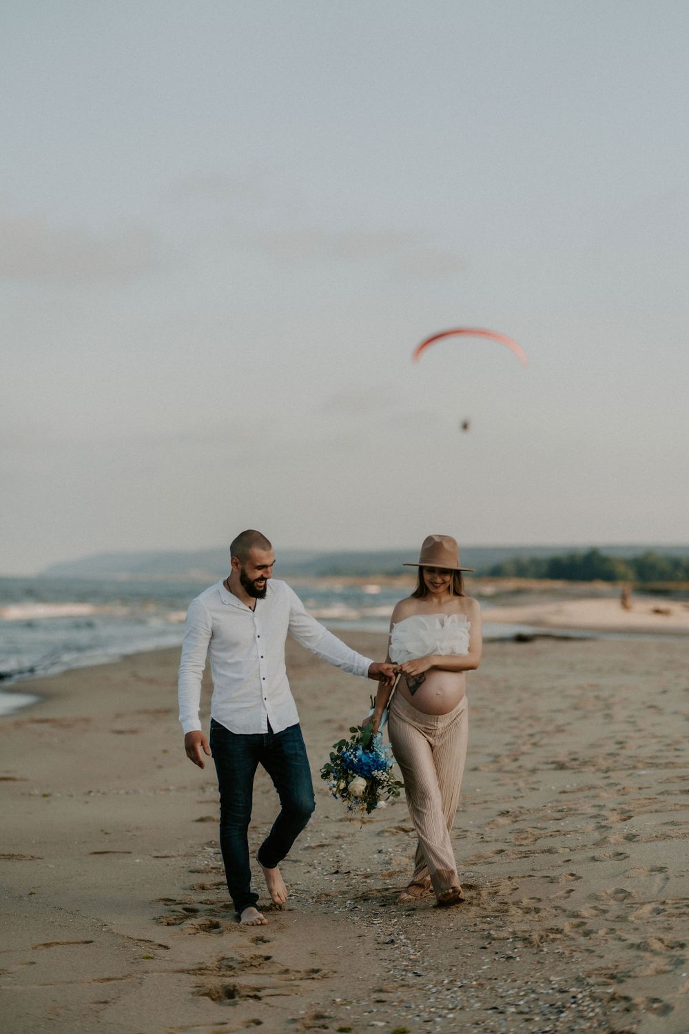 Couple playfully interacts on sandy beach during maternity session.