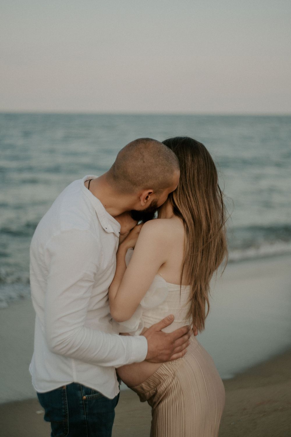 Intimate beach maternity session captures couple's tender embrace at sunset.