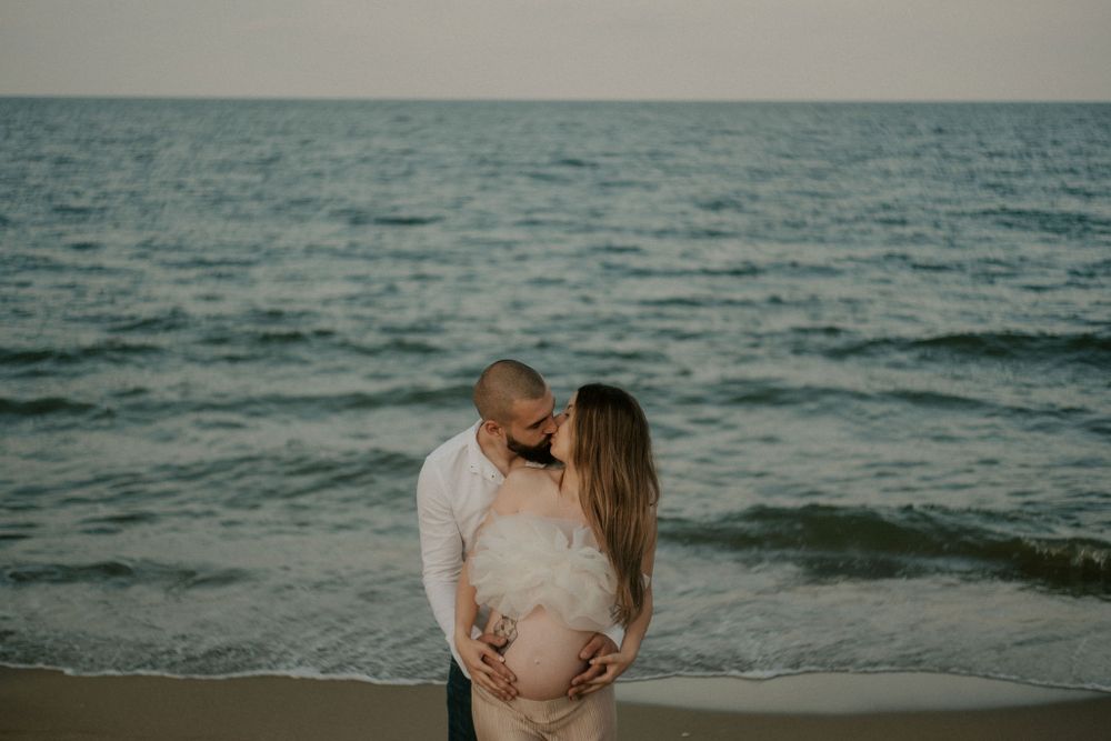 A couple embraces on a scenic beach at sunset with mountains in the background.