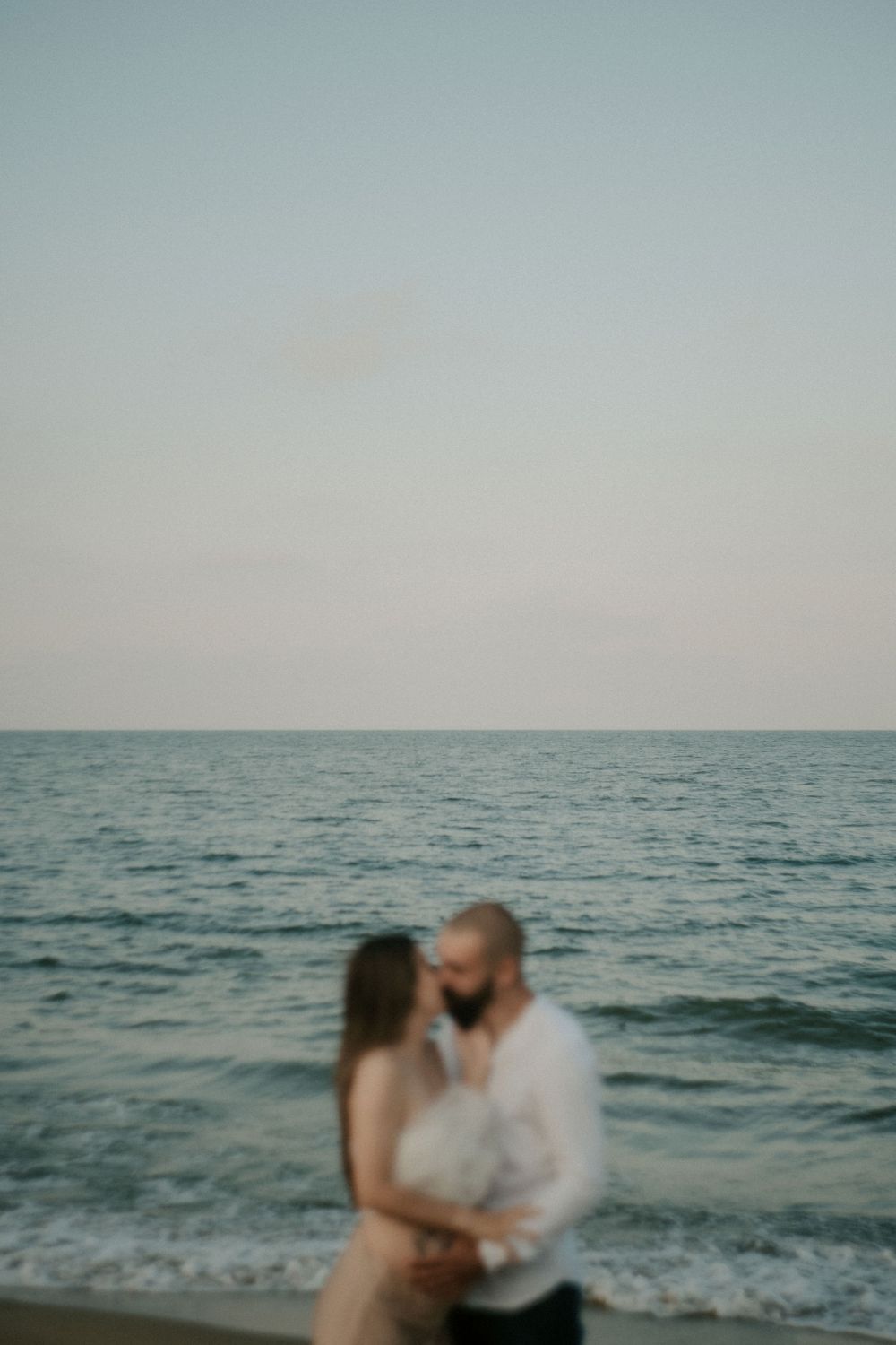 Romantic couple shares an intimate moment on a beach with ocean waves behind them.