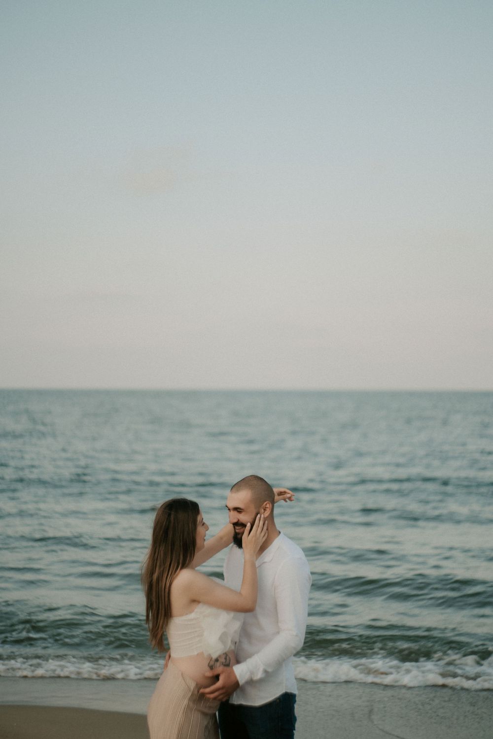 Dancing couple shares a tender moment by the ocean during golden hour.