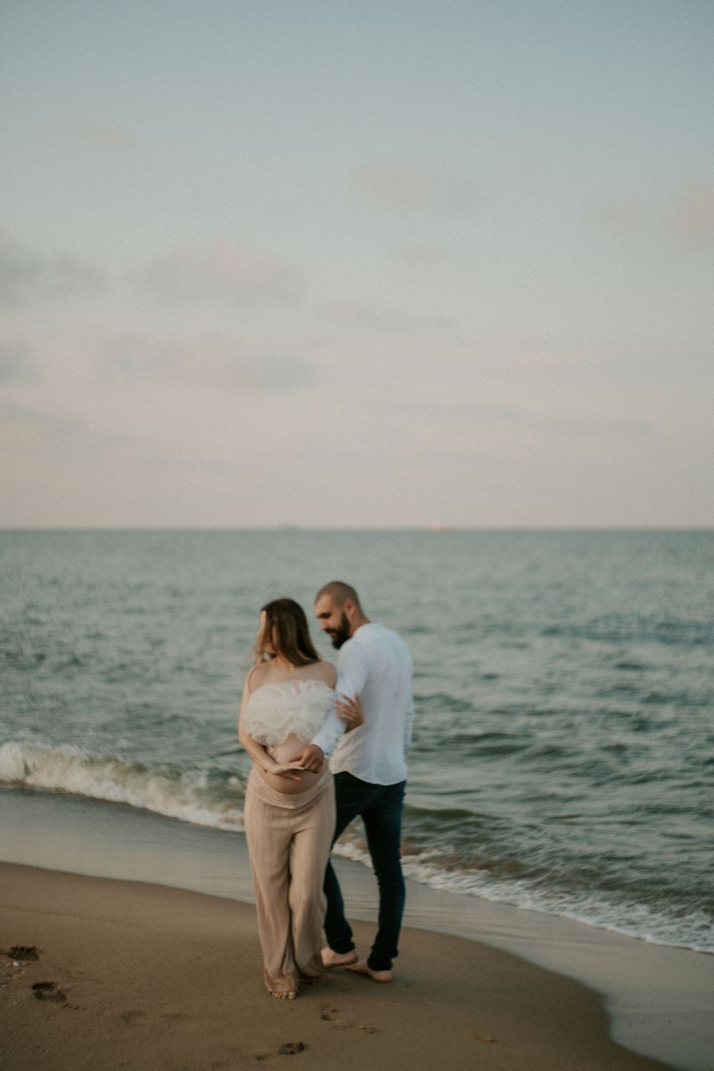 Couple dances playfully together on a sandy beach with waves rolling in.