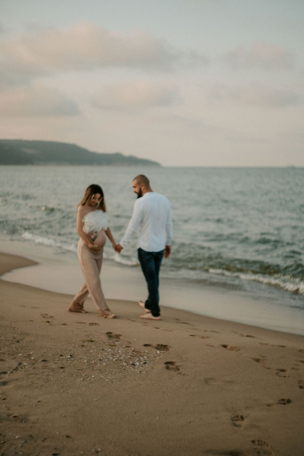 Two people dance and laugh together on a beach with mountains visible in the distance.