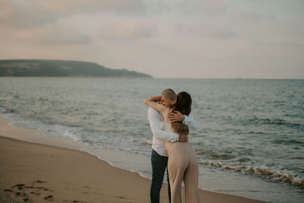Two people share an intimate embrace on a beach at dusk.