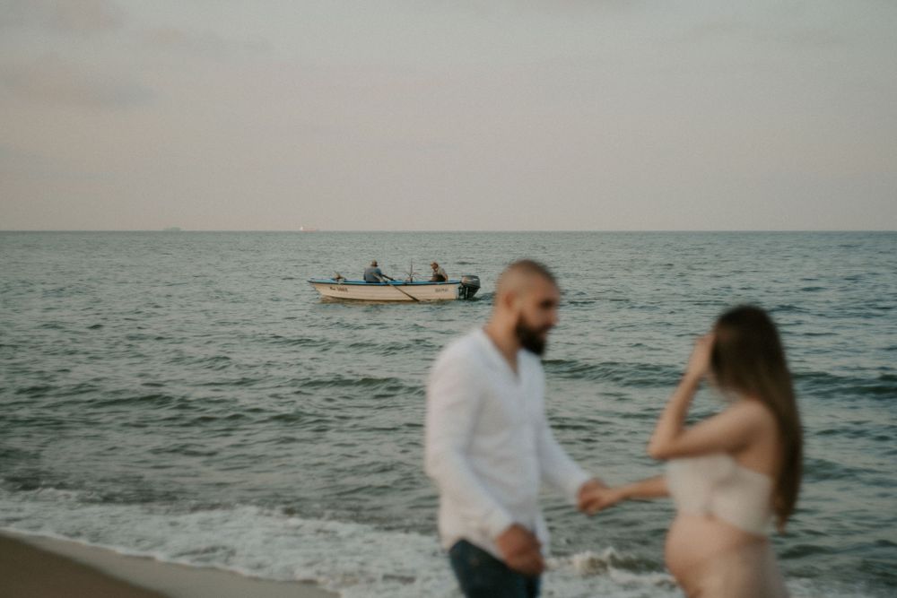 Couple dances joyfully on the beach with ocean waves in the background.