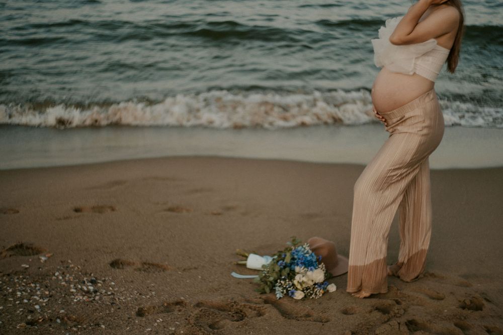 Romantic maternity photoshoot at sunset on a sandy beach with waves crashing in the background.
