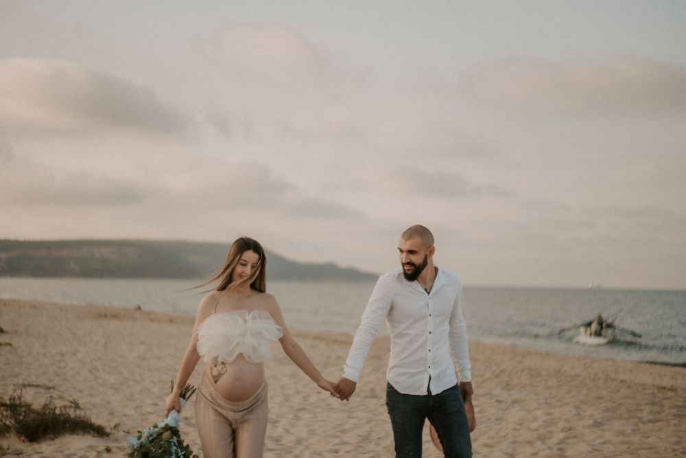 Couple walking hand in hand along a misty beach during golden hour.
