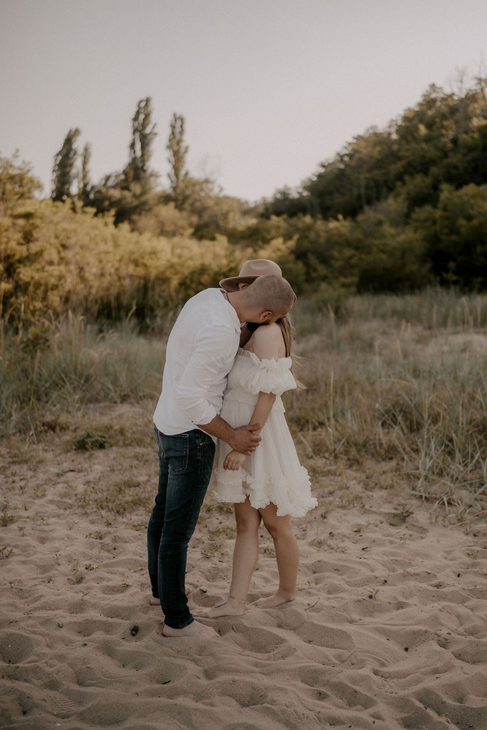 Romantic couple interacting on sandy beach with natural foliage in background.