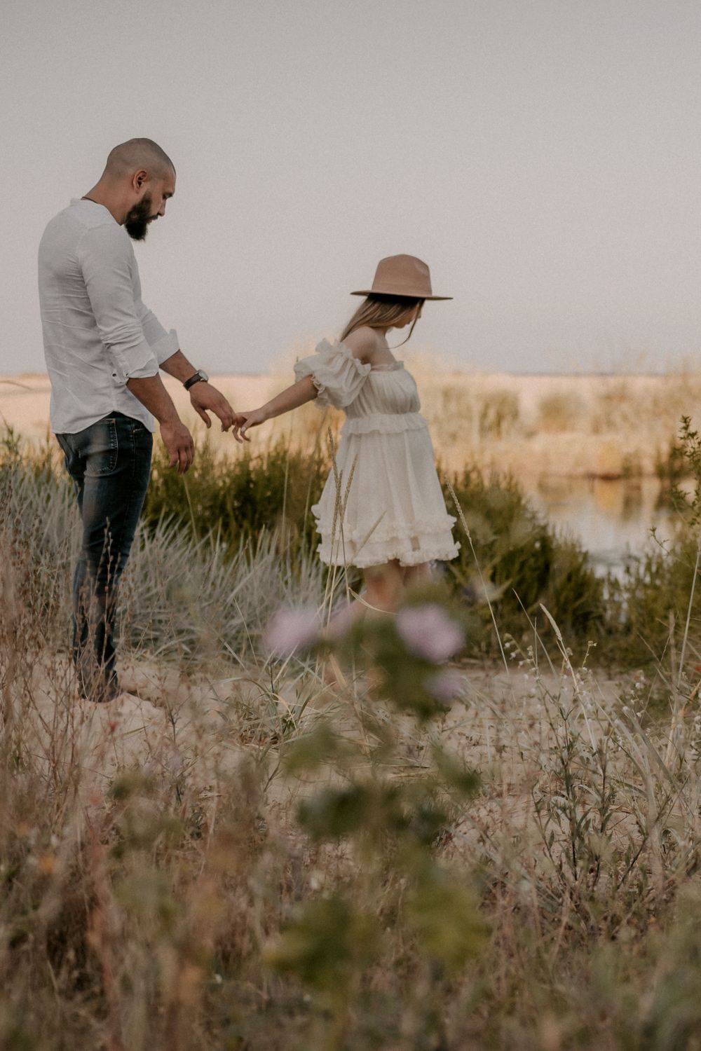 Couple walking through tall grass and wildflowers during golden hour photoshoot.
