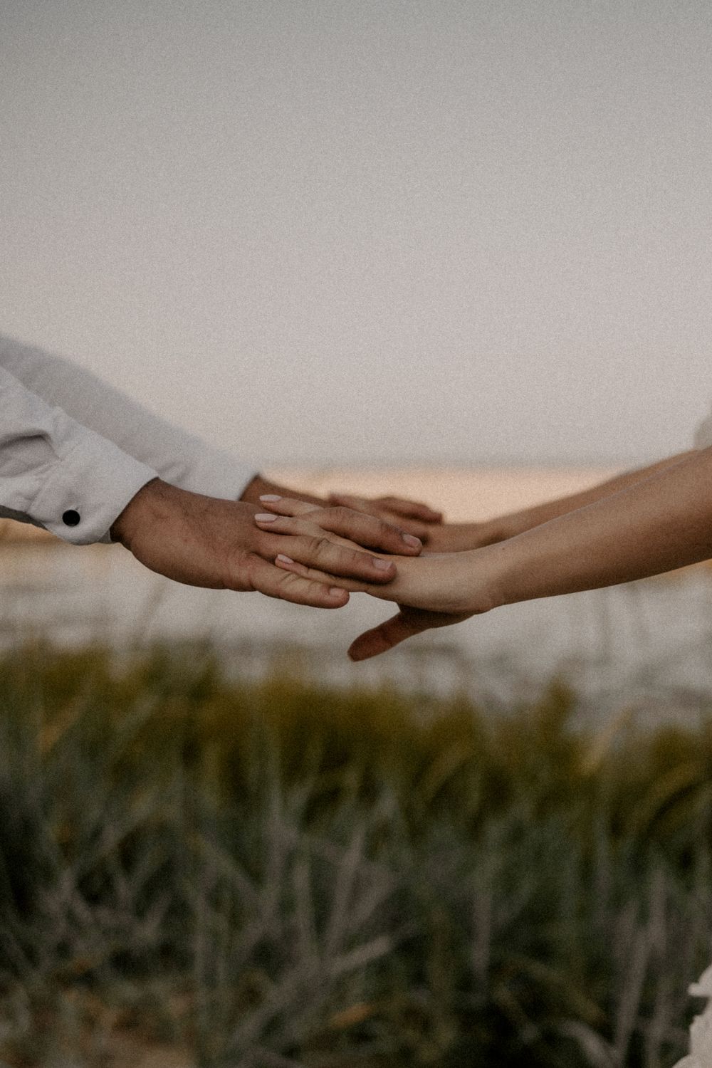 Two hands tenderly touch in an intimate moment against a natural outdoor backdrop.