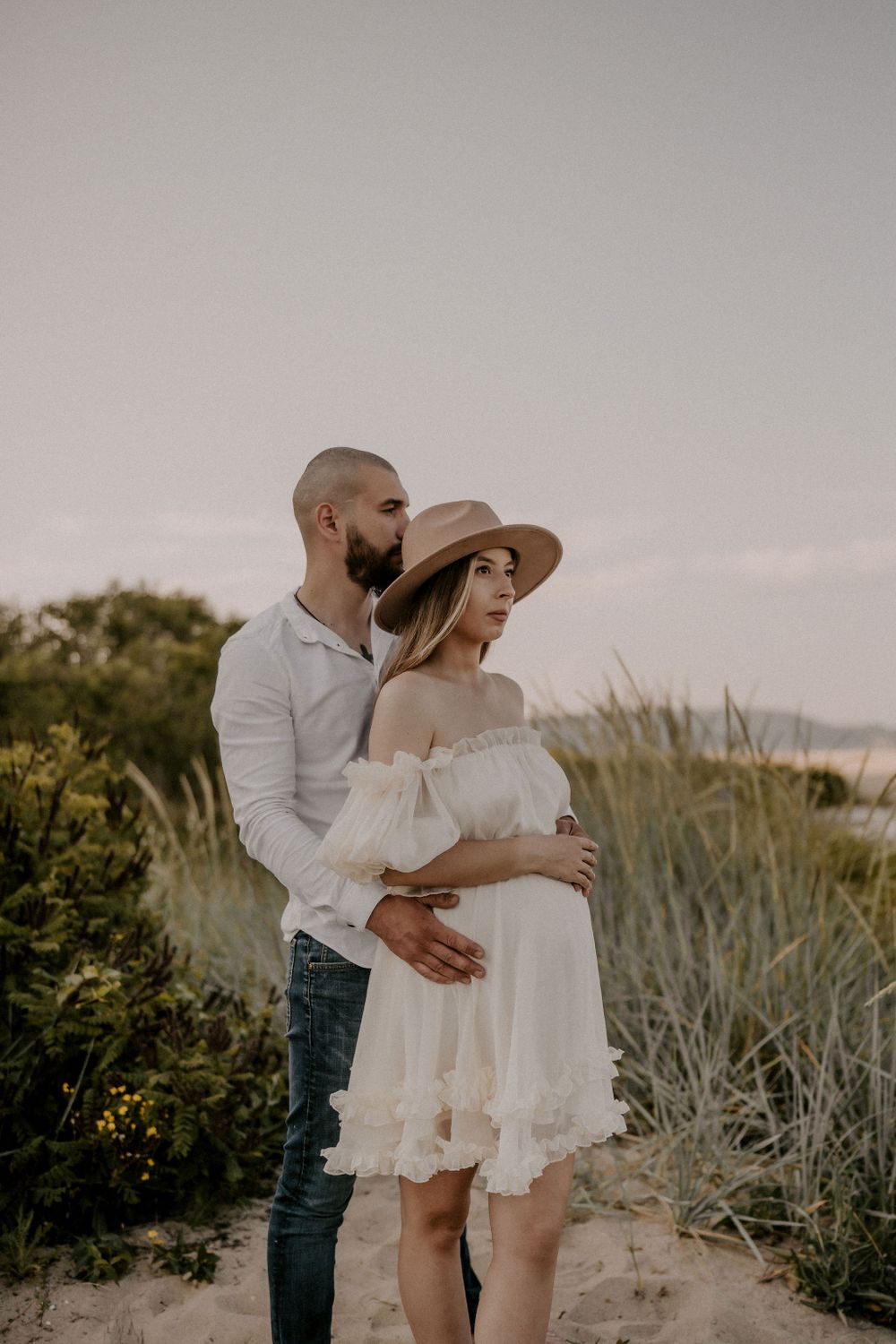 A tender embrace captured on a sandy beach path surrounded by coastal vegetation.