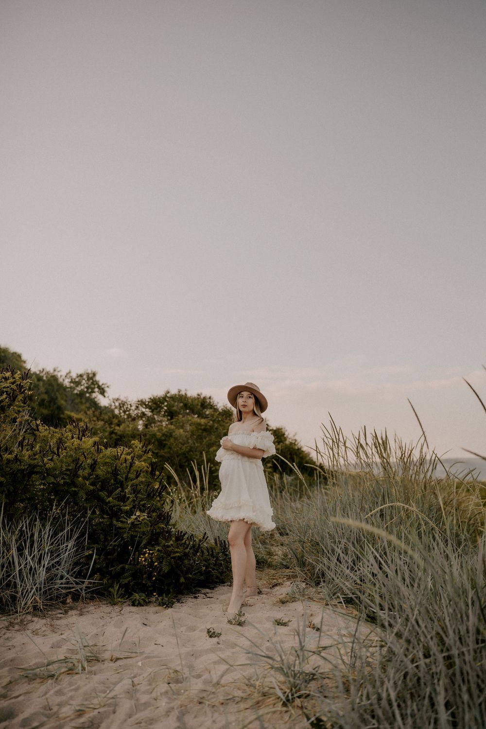 A dreamy coastal portrait featuring a white dress and wide-brimmed hat.