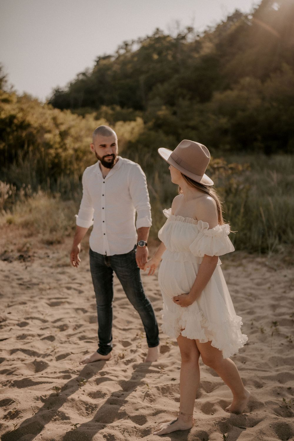 A couple playfully walking together on sandy beach during golden hour sunset.