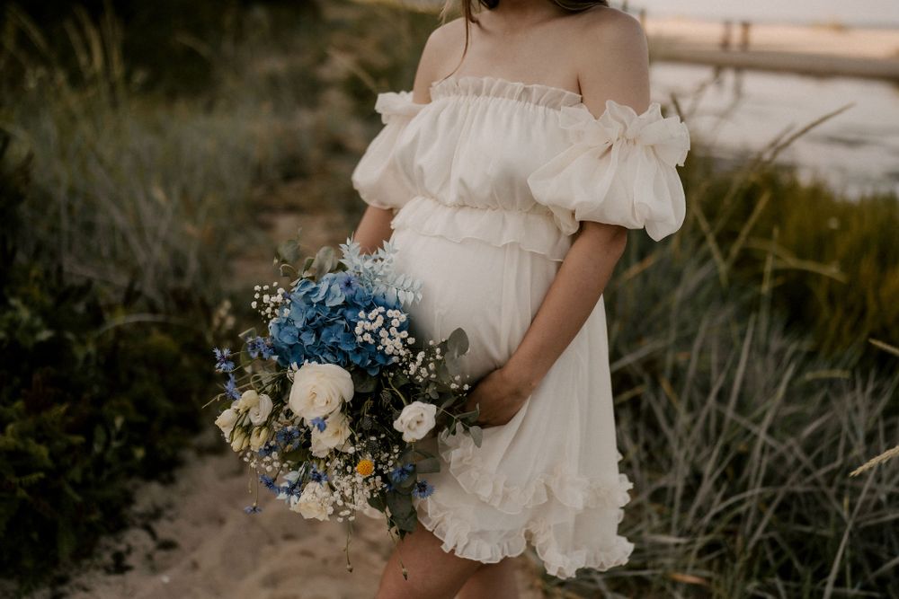 A romantic couple stands on a sandy beach at sunset holding a delicate bouquet with blue flowers.