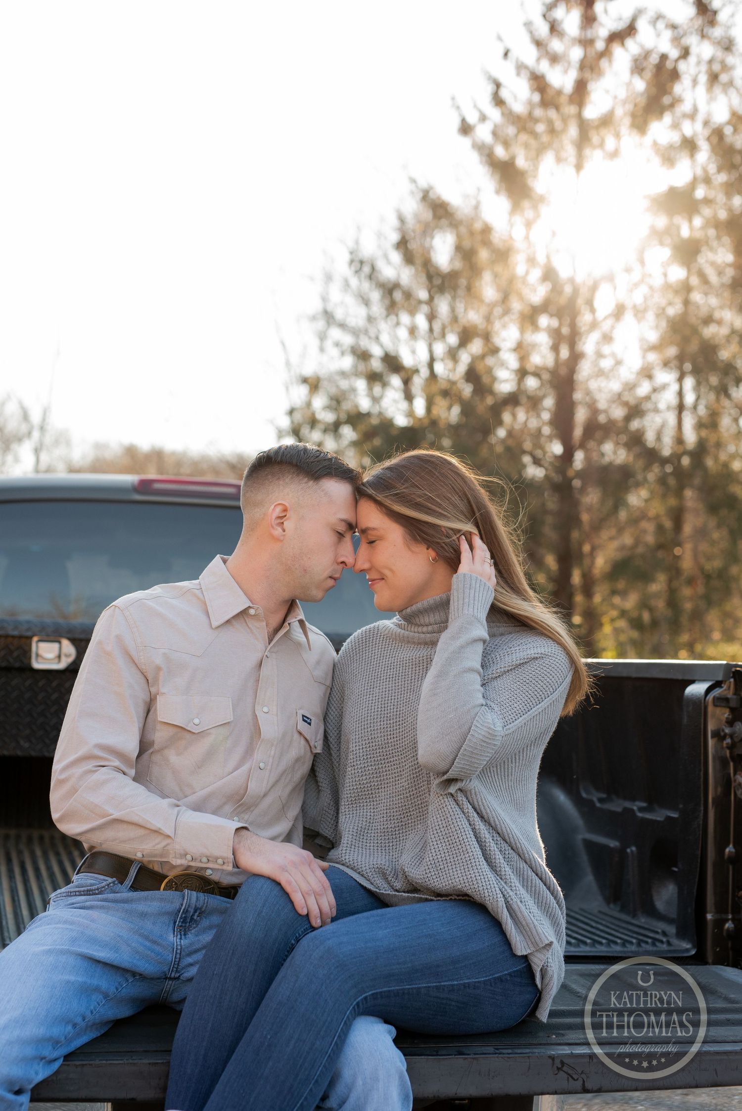 Couple in casual wear sharing a tender moment in the back of a pickup truck at sunset.