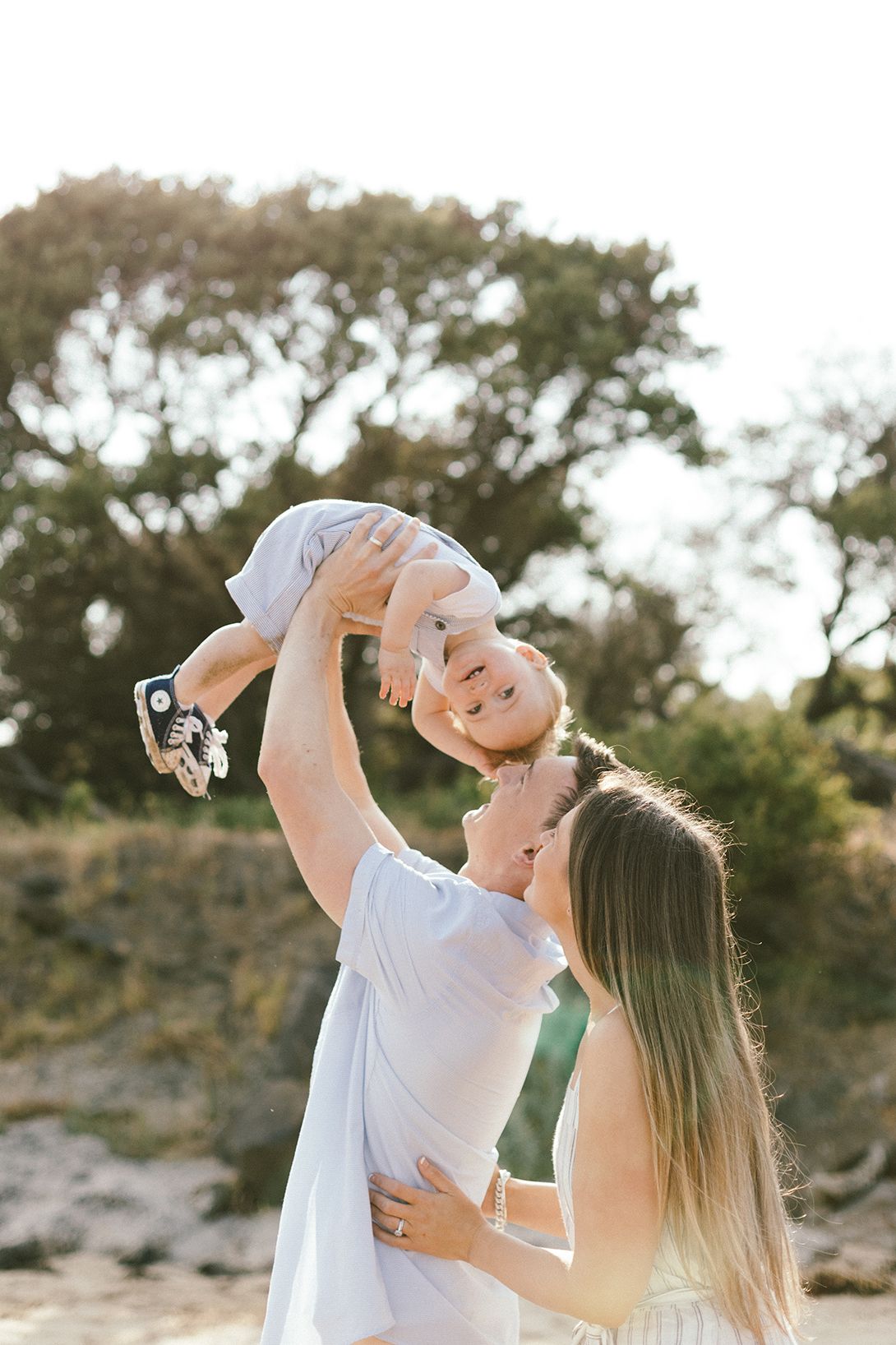 A joyful family moment captured on a beach with trees in the background during golden hour.