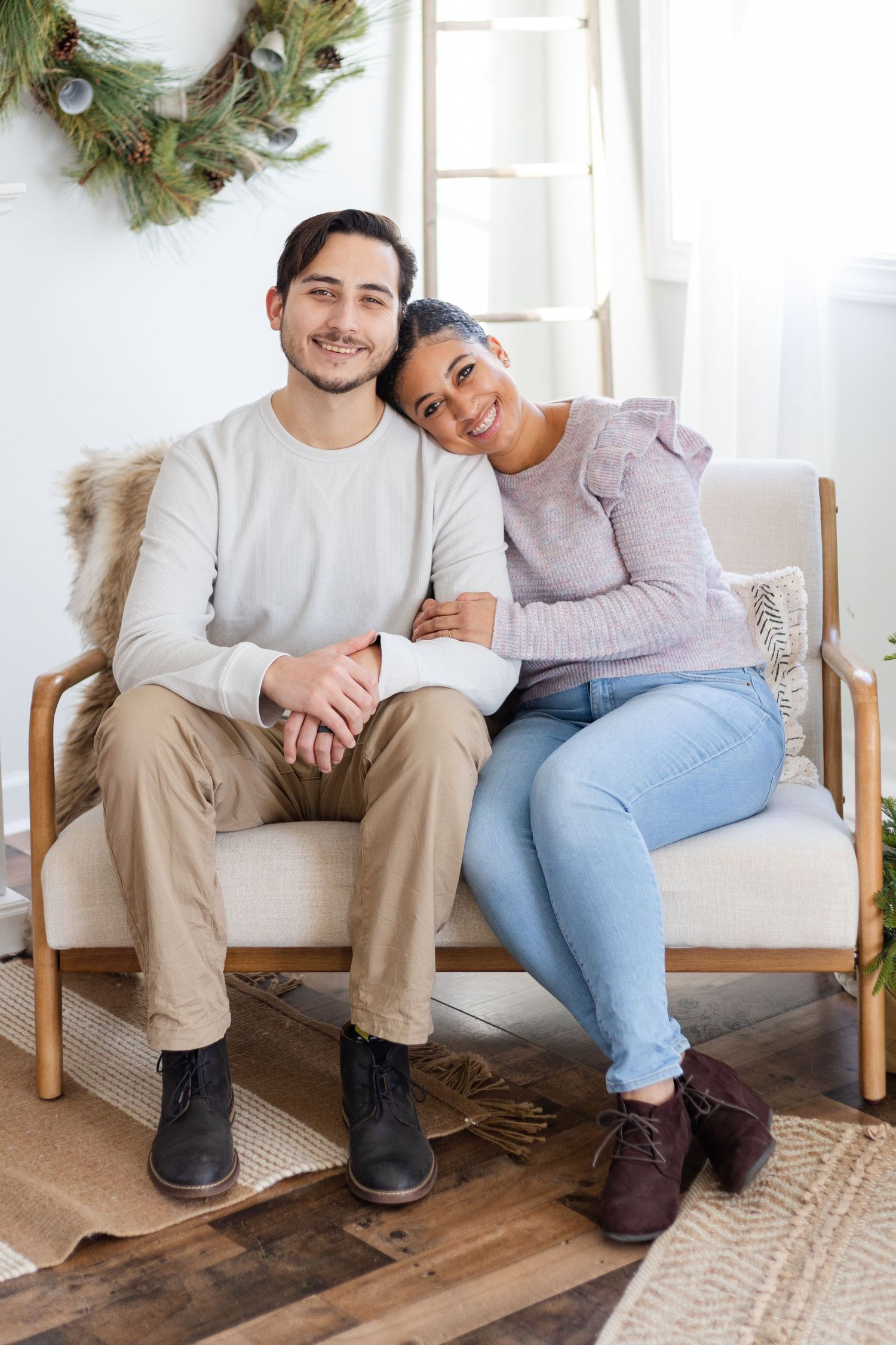 Couple relaxing together on wooden bench with holiday wreath decoration in background.