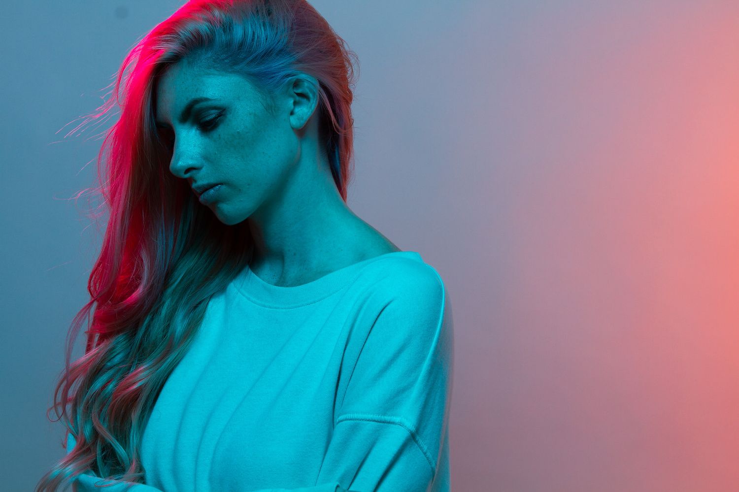 Portrait in neon lighting with vibrant pink hair against blue and red backdrop.