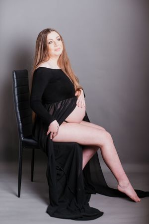 Artistic maternity portrait on a chair wearing a dramatic black flowing gown.