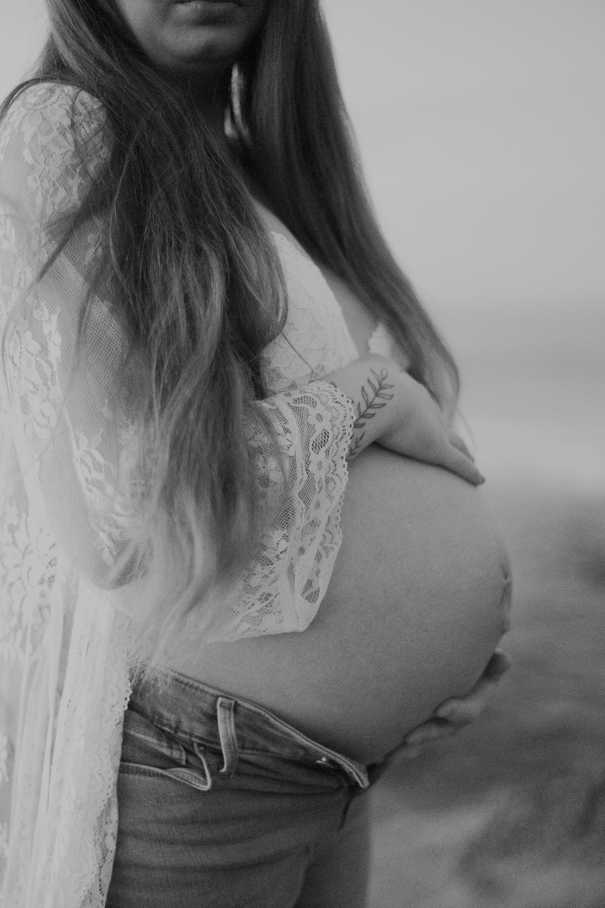 Black and white side profile of pregnant belly with lace detail and denim.