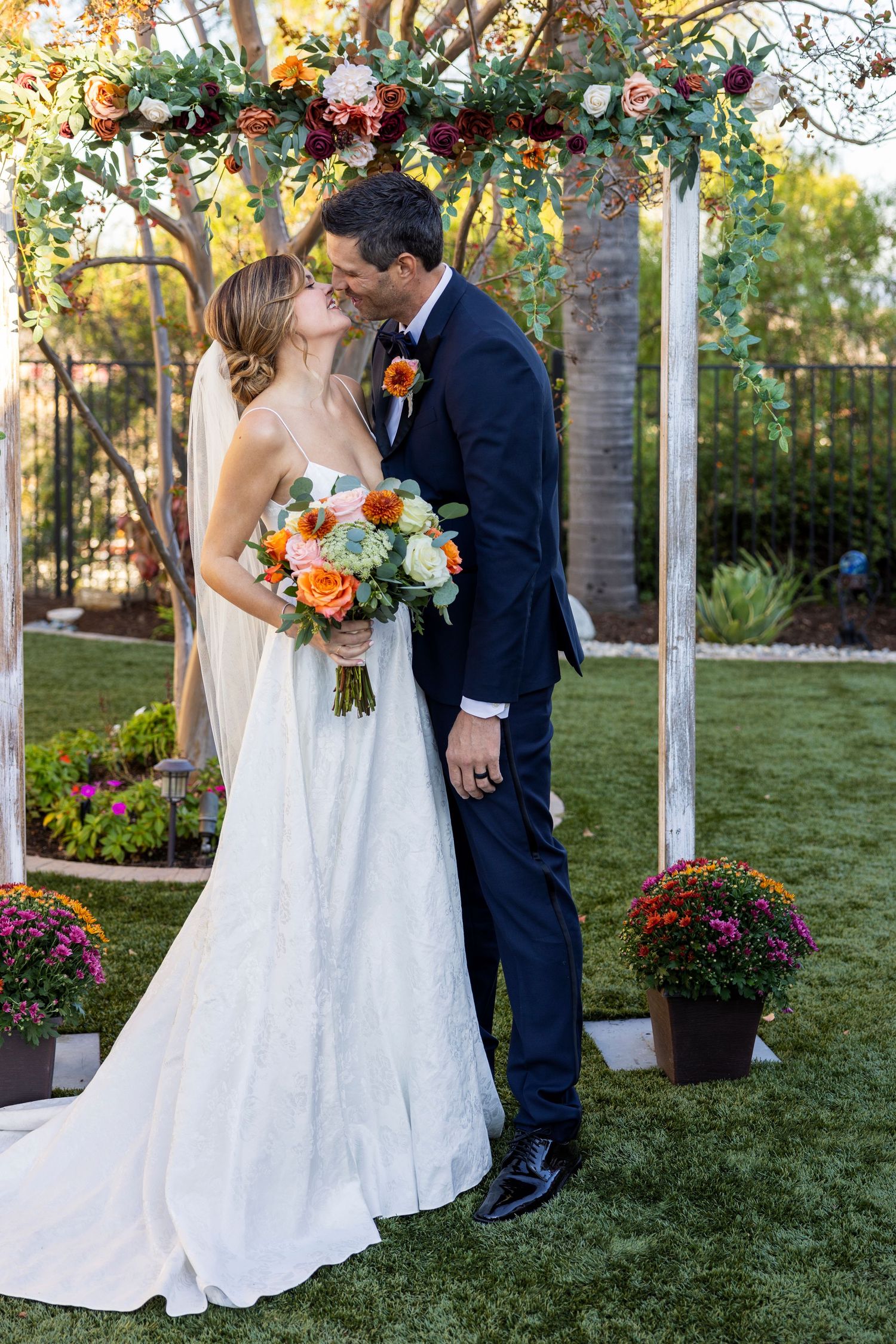 Orange County photographer captures Bride and groom sharing a kiss under a floral wedding arch in a garden setting.