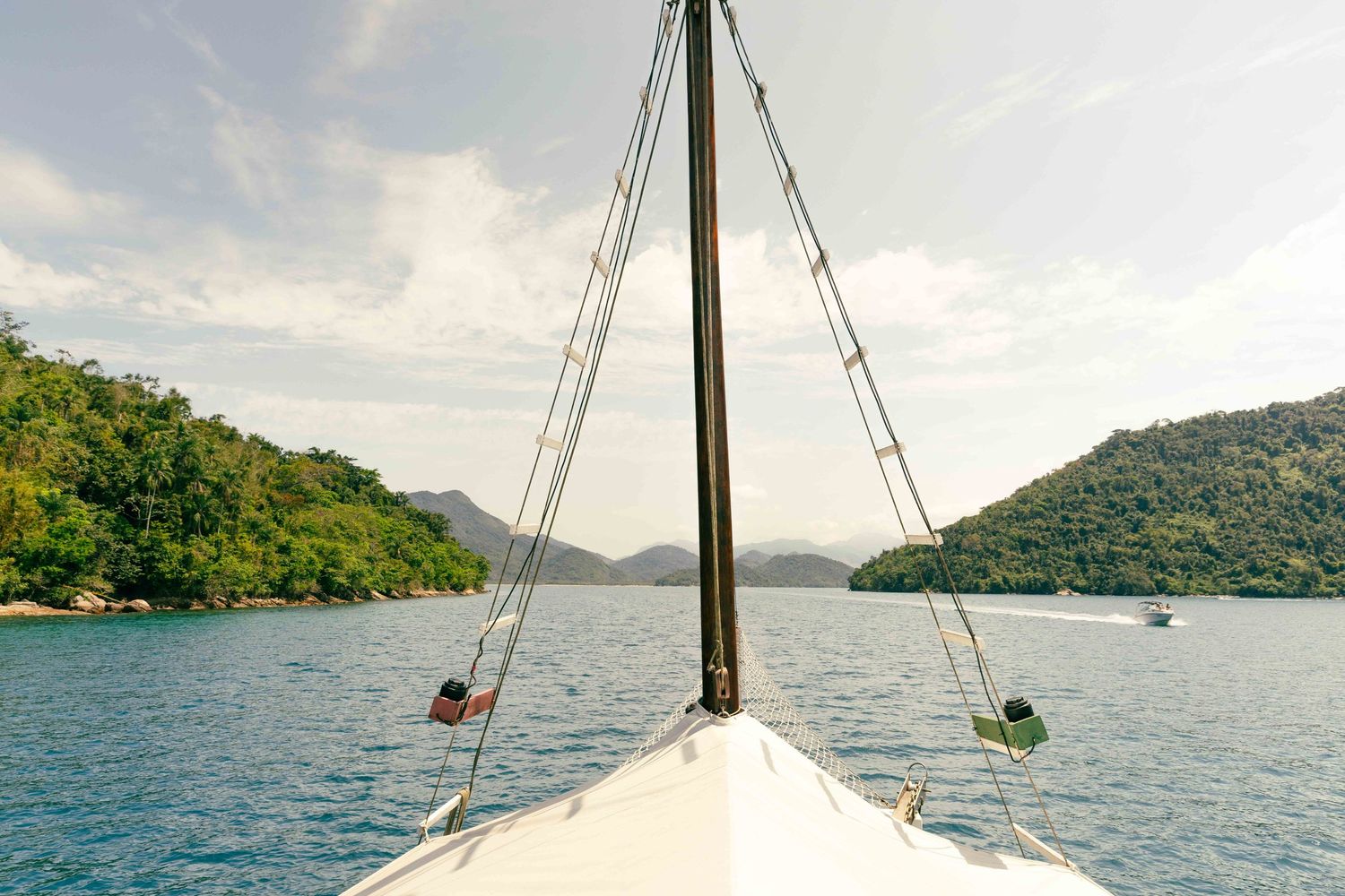 Sailboat bow pointing towards tropical islands with turquoise water and mountain views.