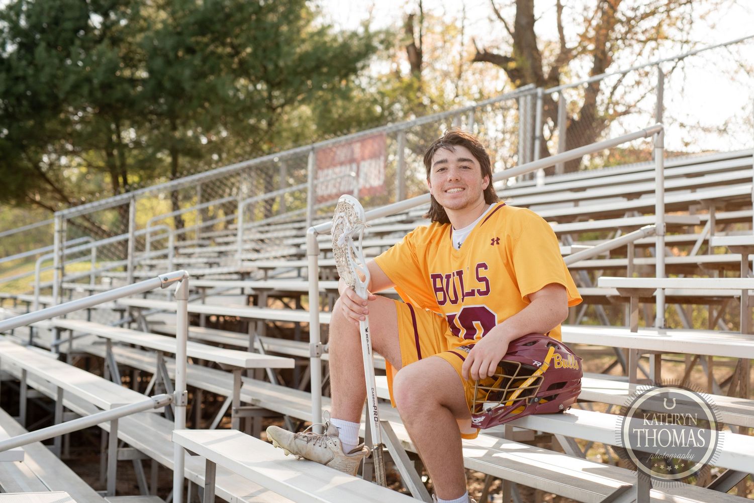 Player in yellow Bulls uniform sits on metal bleachers during golden hour.