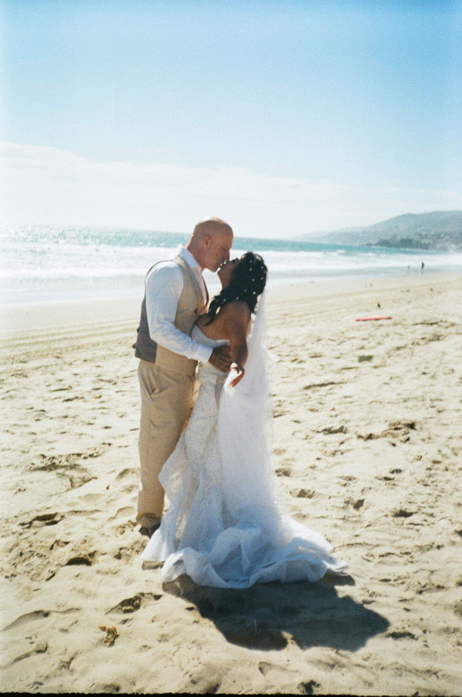 Romantic beach wedding photoshoot featuring a couple embracing on sandy shoreline with ocean waves in background.