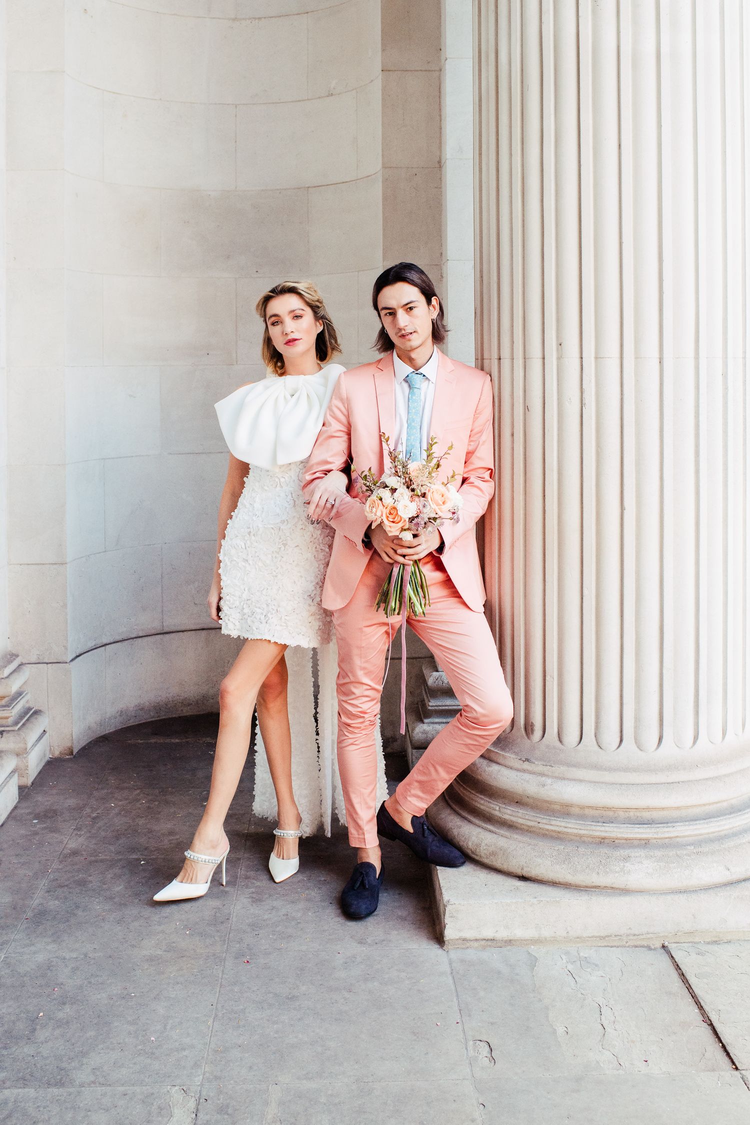 Wedding couple in London posing against classical marble columns in a stylish photoshoot series.