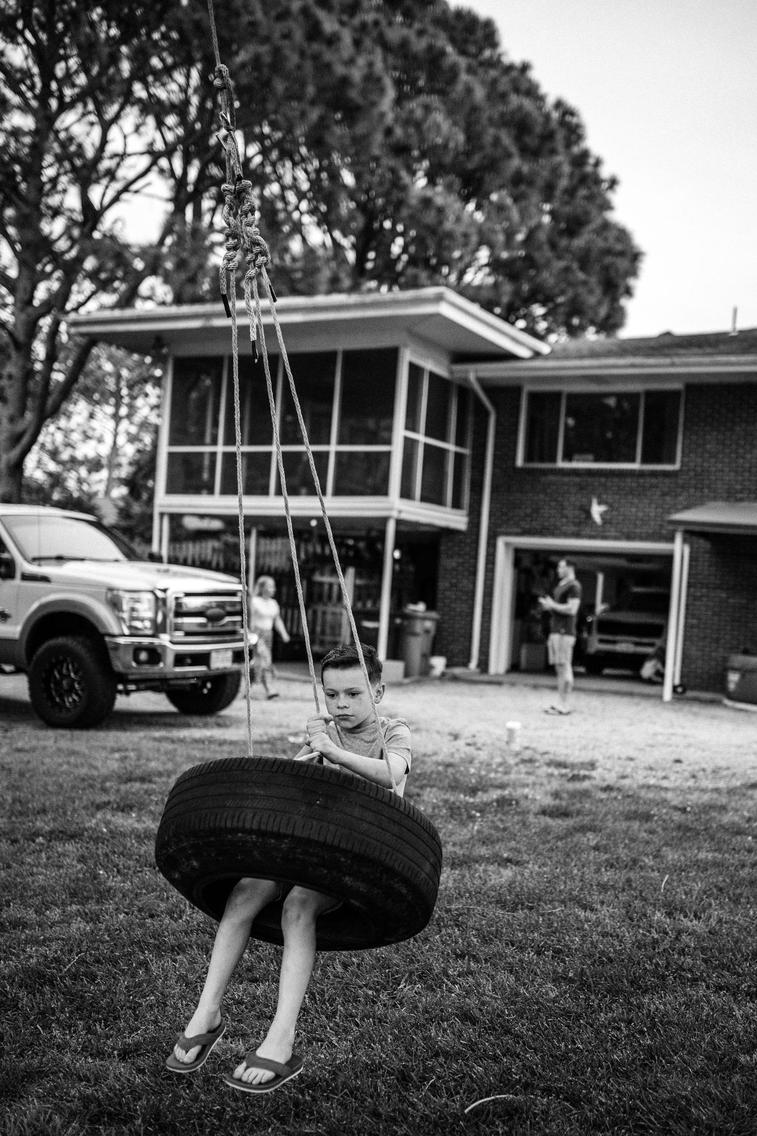 little boy in tire swing in the backyard of his home in chesapeake, virginia with dad and brother in the background