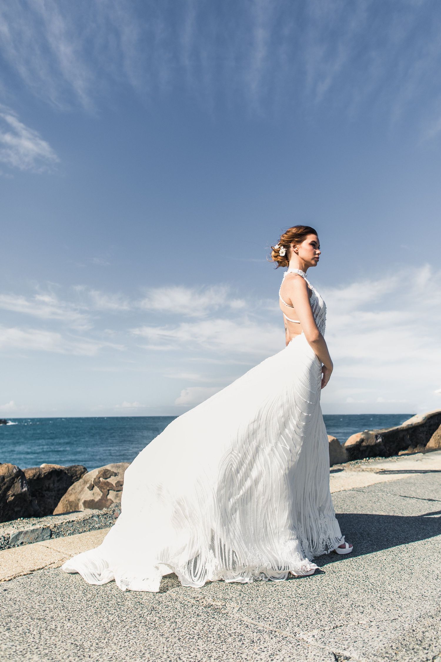 Flowing white dress against coastal rocks and blue ocean backdrop.