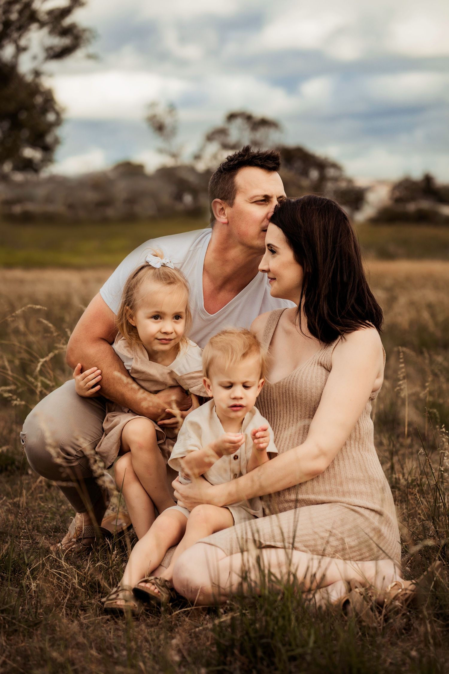 A family with young children poses together in a field during golden hour.