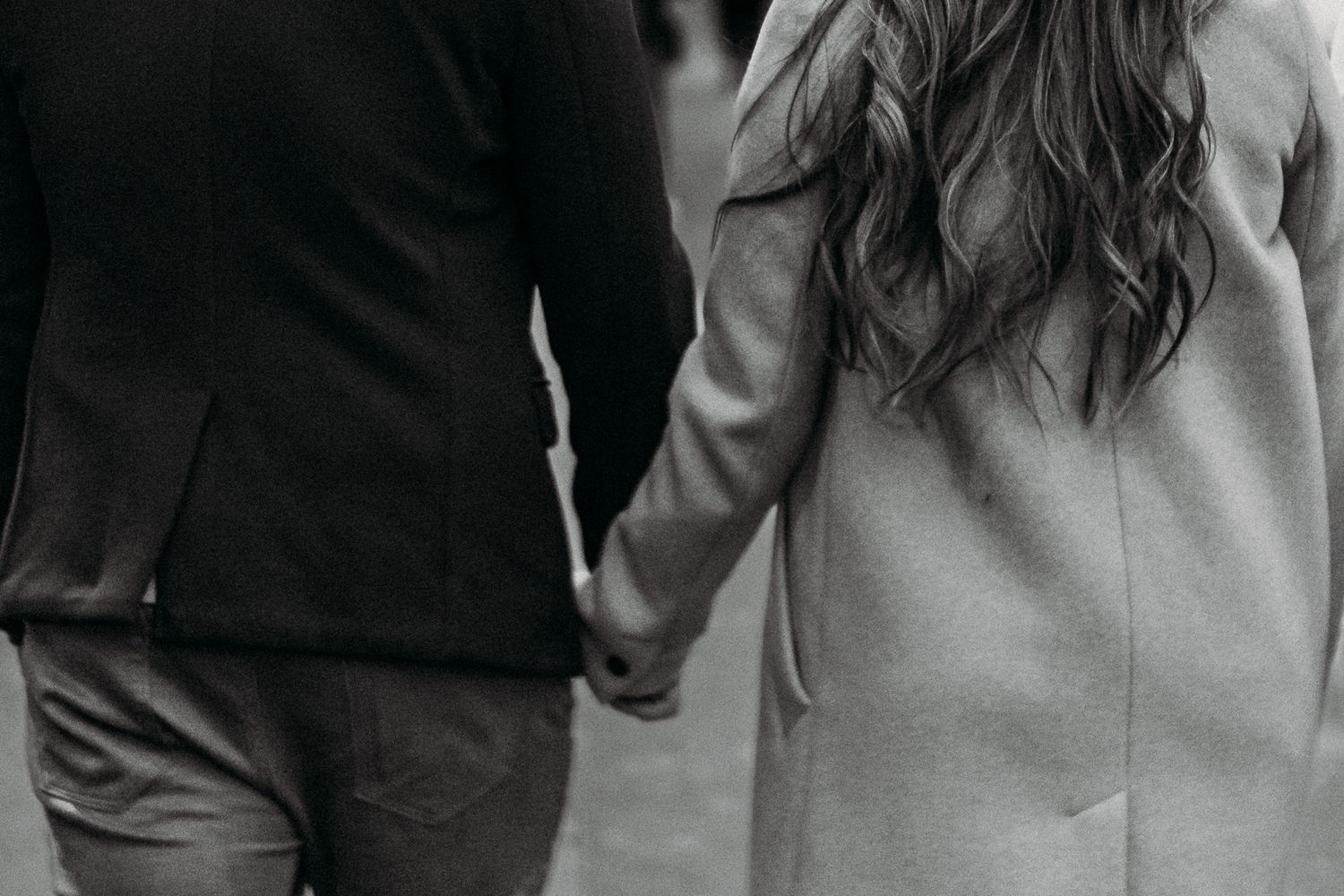 Close-up black and white shot of two people holding hands while walking together.