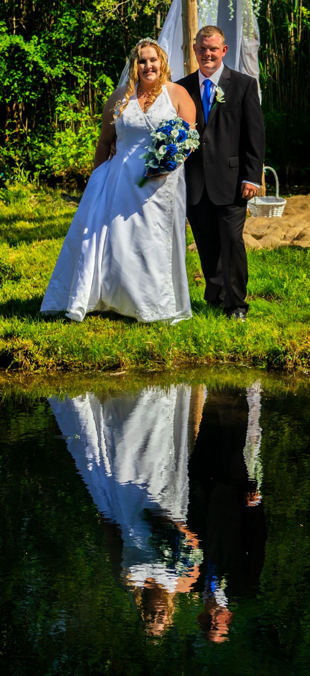 Bride and groom standing at the edge of a pond with their reflection showing