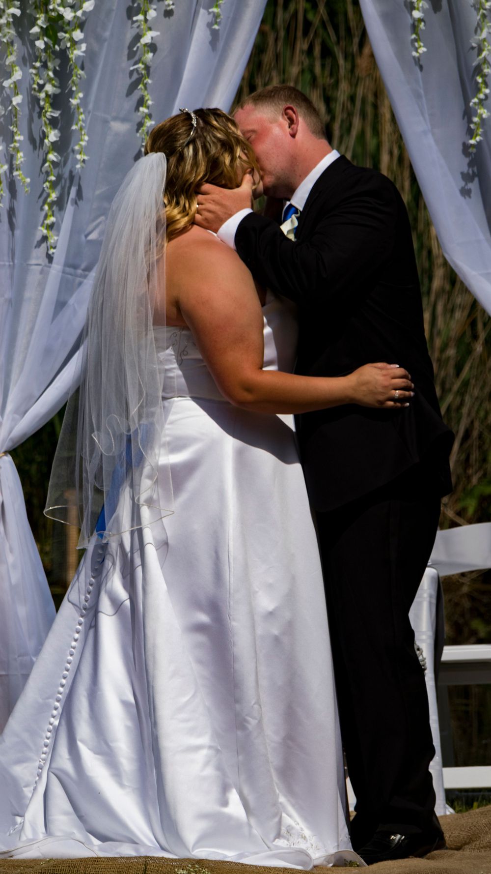 Bride and groom's first kiss in front of a white draped archway outsides