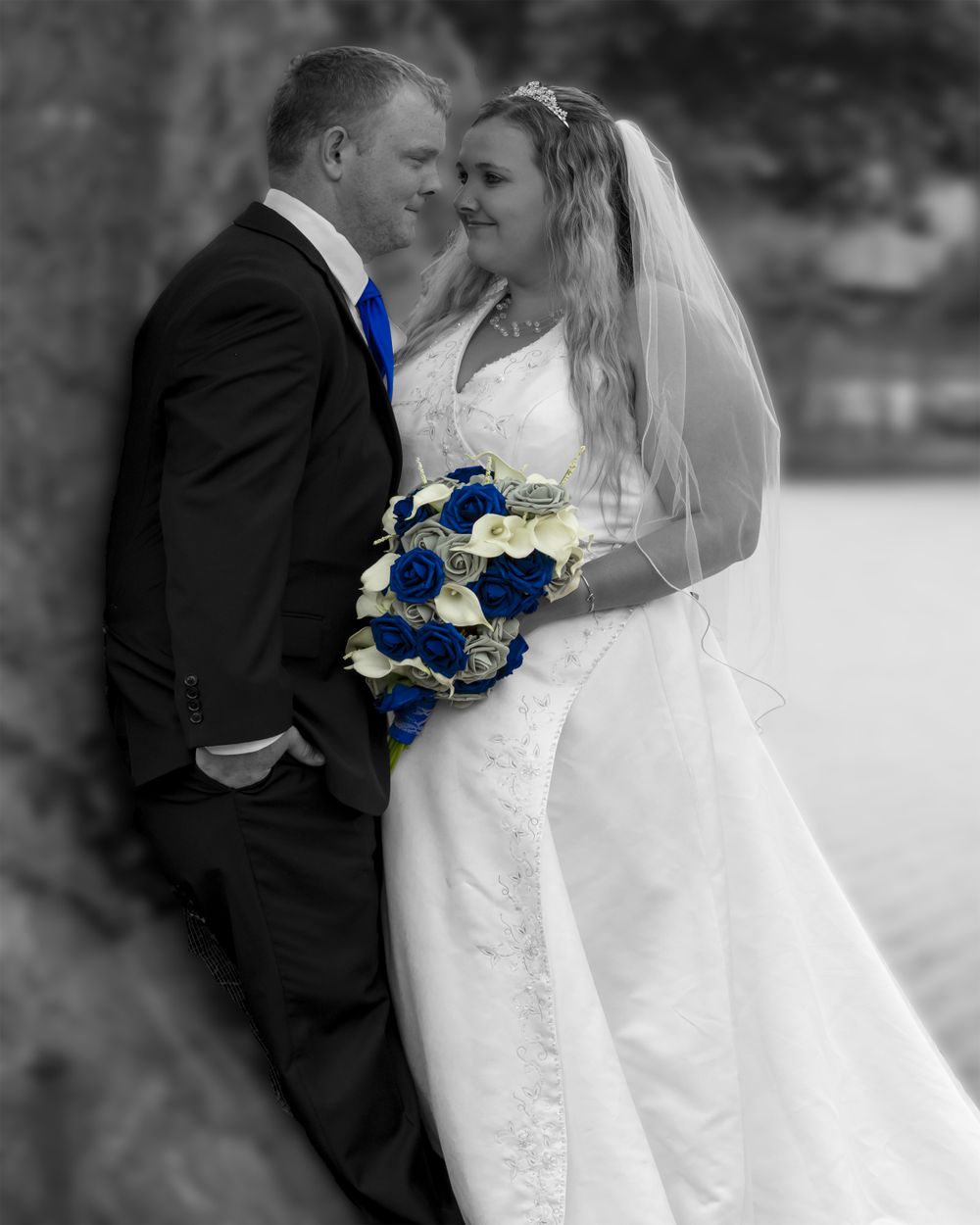 Bride and groom looking at each other leaning against a tree
