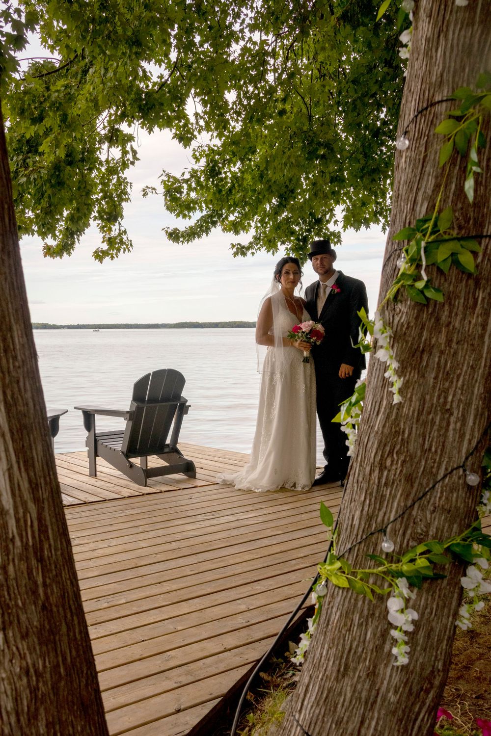 Bride and groom standing on a dock framed in tree trunks