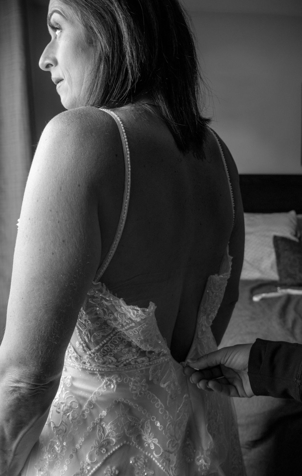 Bride standing in front of a window putting her dress on
