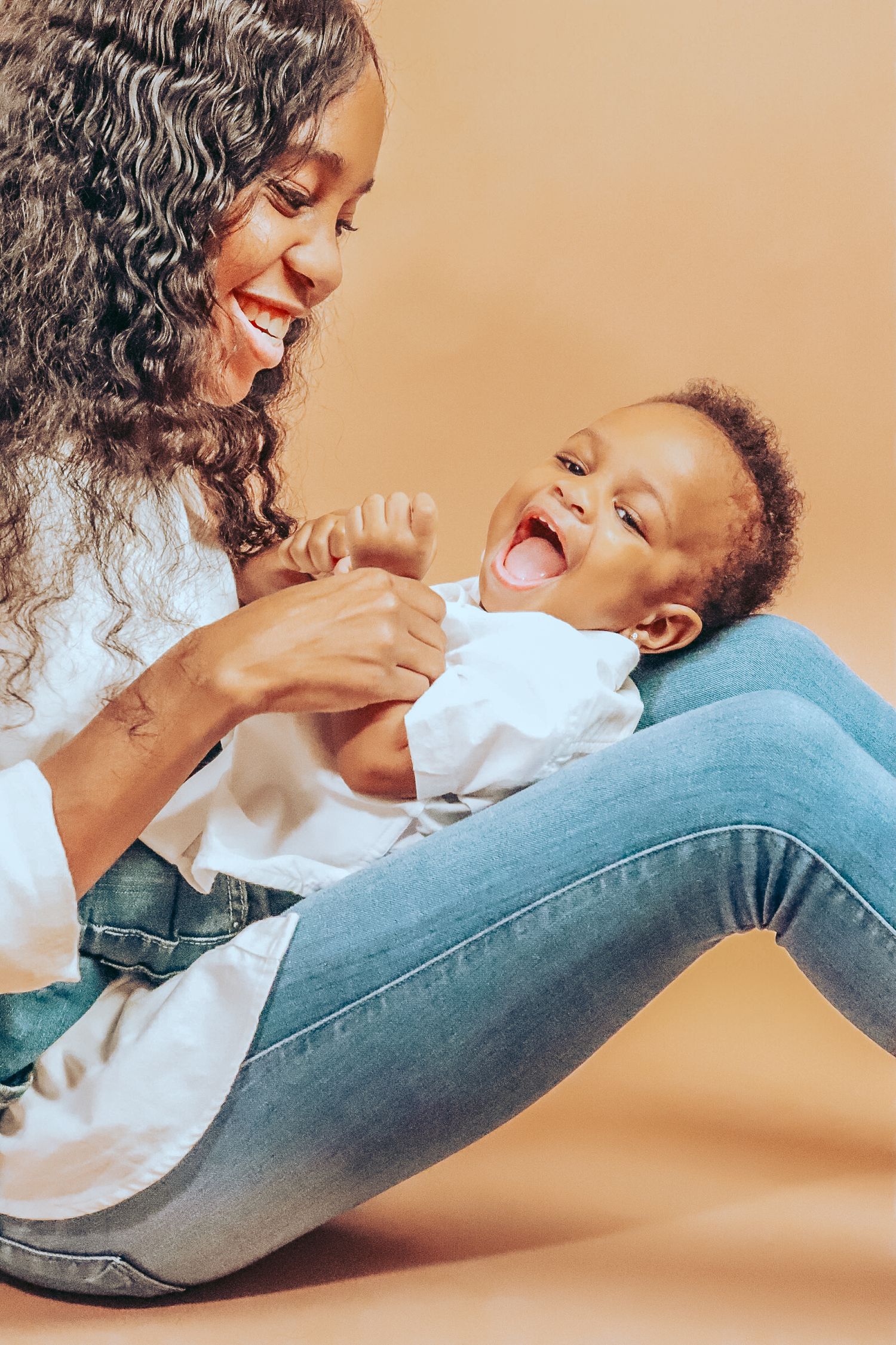 Joyful Black mother laughing and playing with her happy giggling baby on a beige background.
