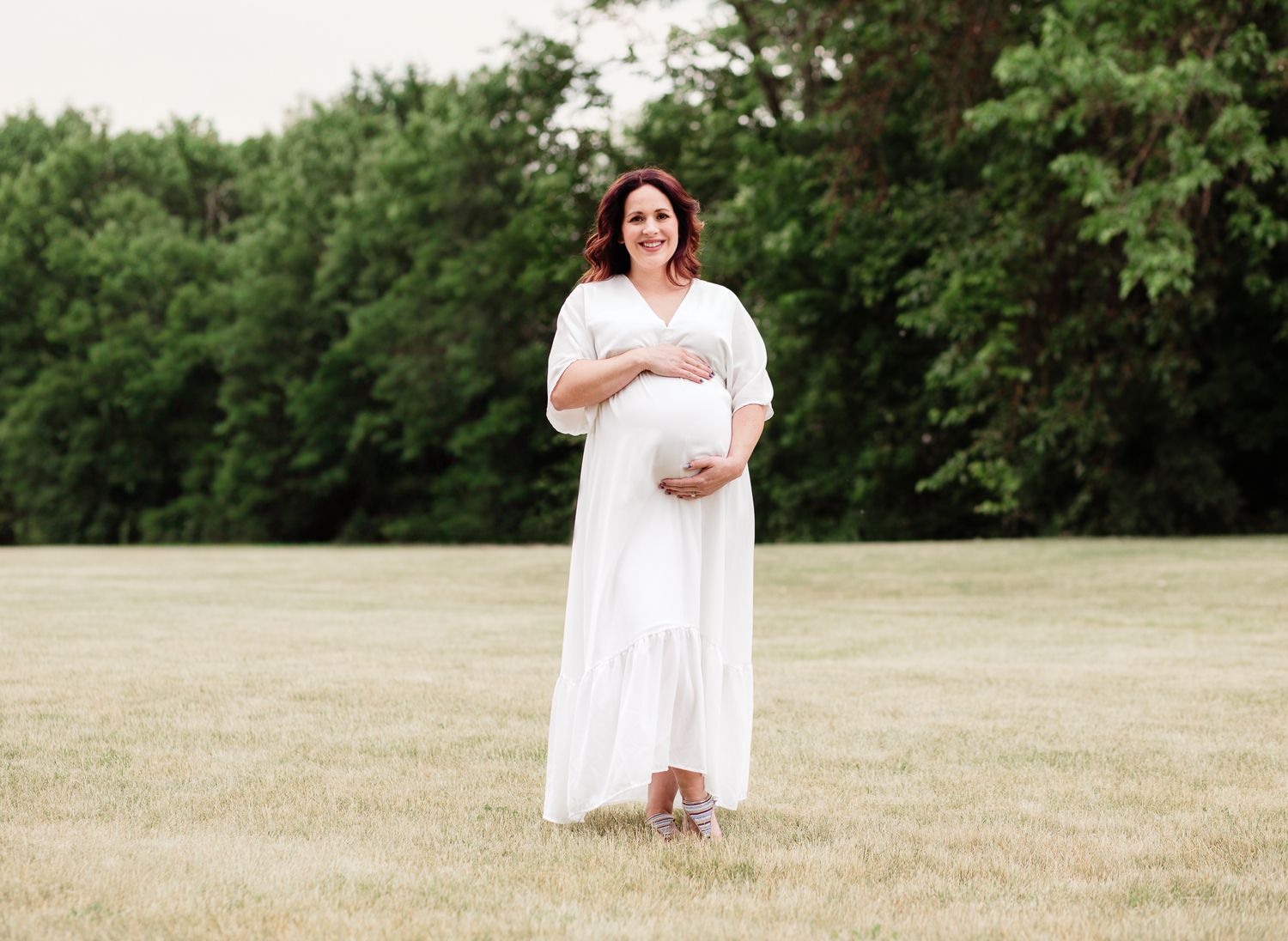 outdoor maternity photo in Bartlett, IL pregnant woman wearing white long dress smiling at the camera