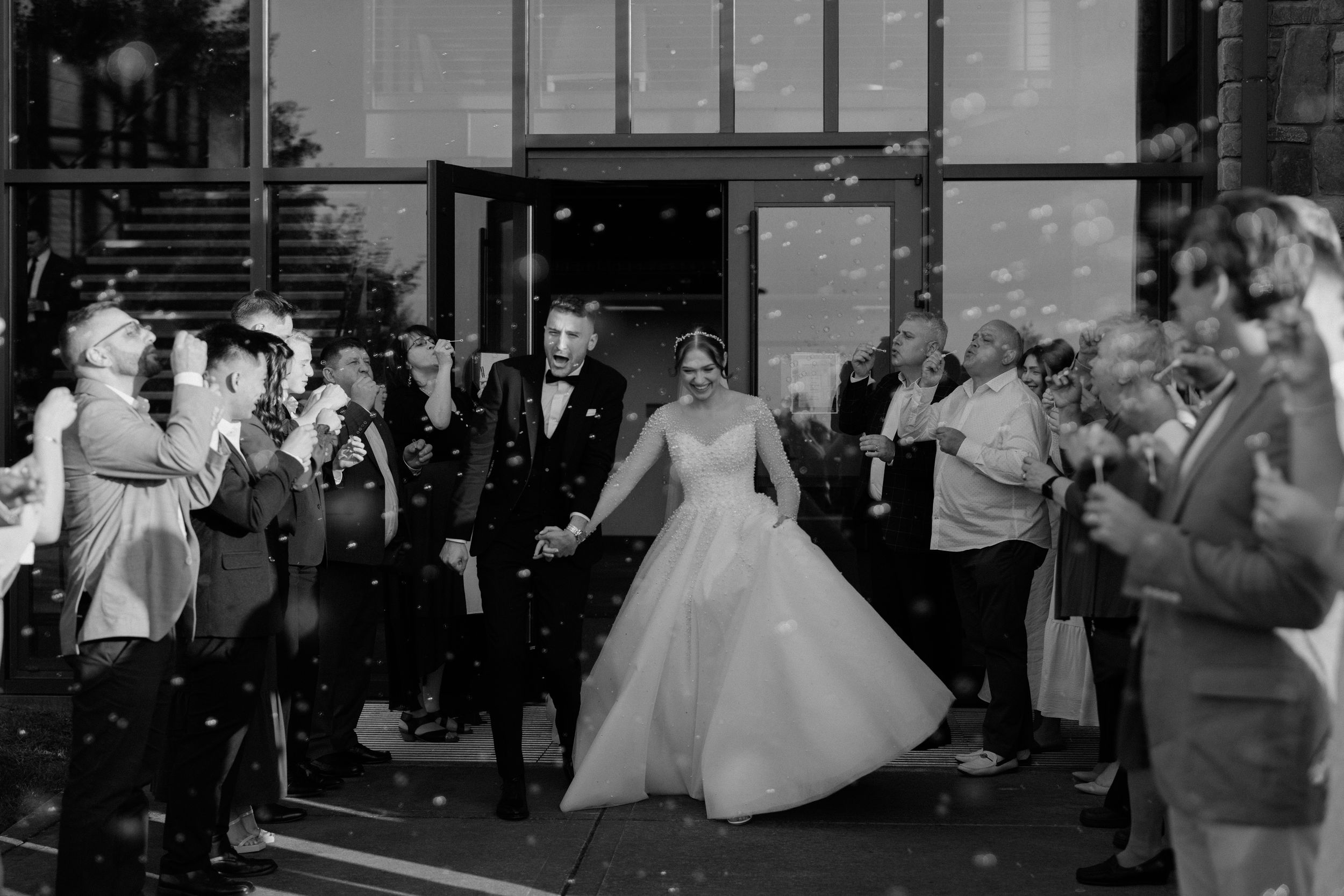 A bride in a flowing white dress twirls joyfully during a reception as guests gather around clapping.
