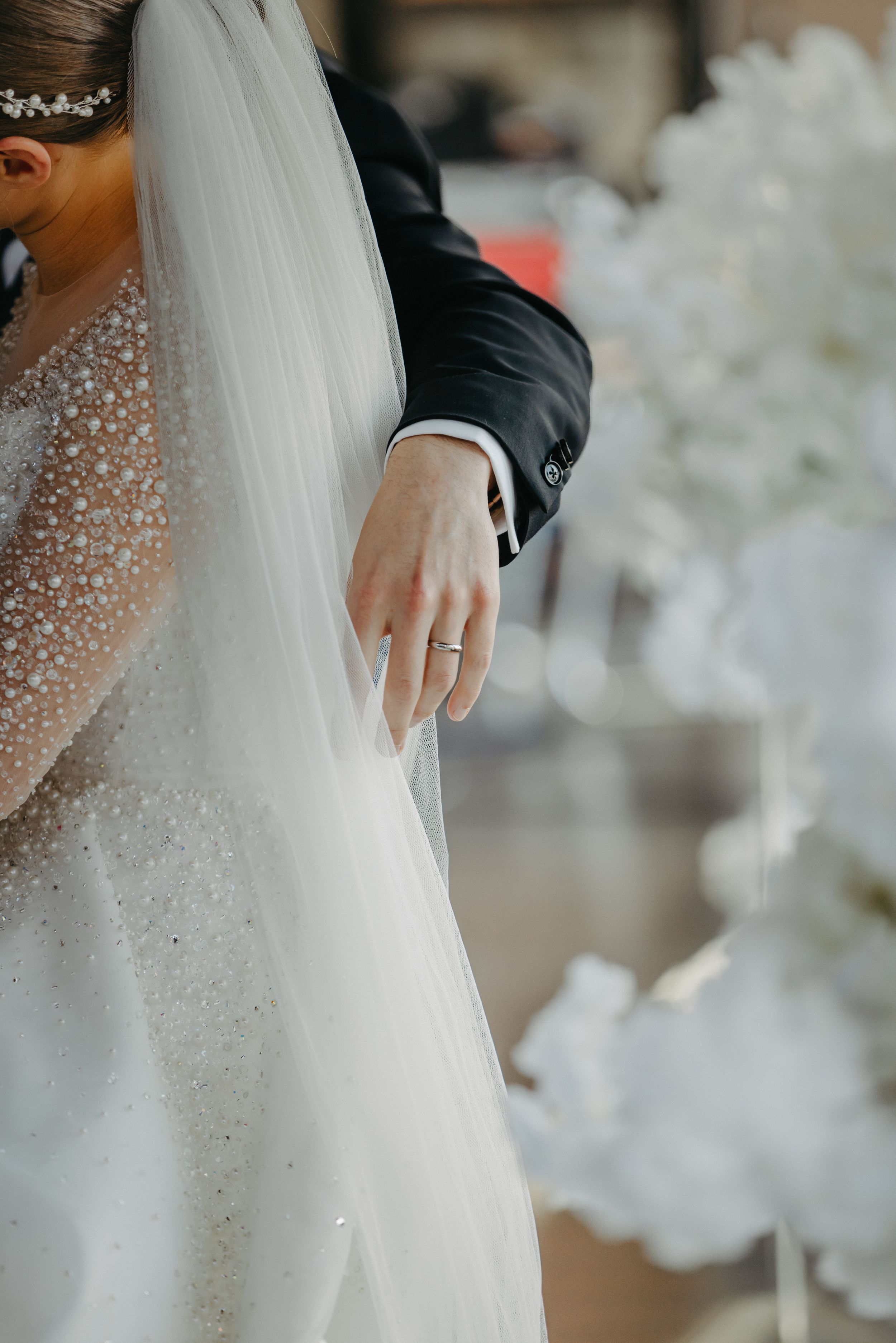 Close-up detail of sparkly wedding dress and veil with white floral decorations.