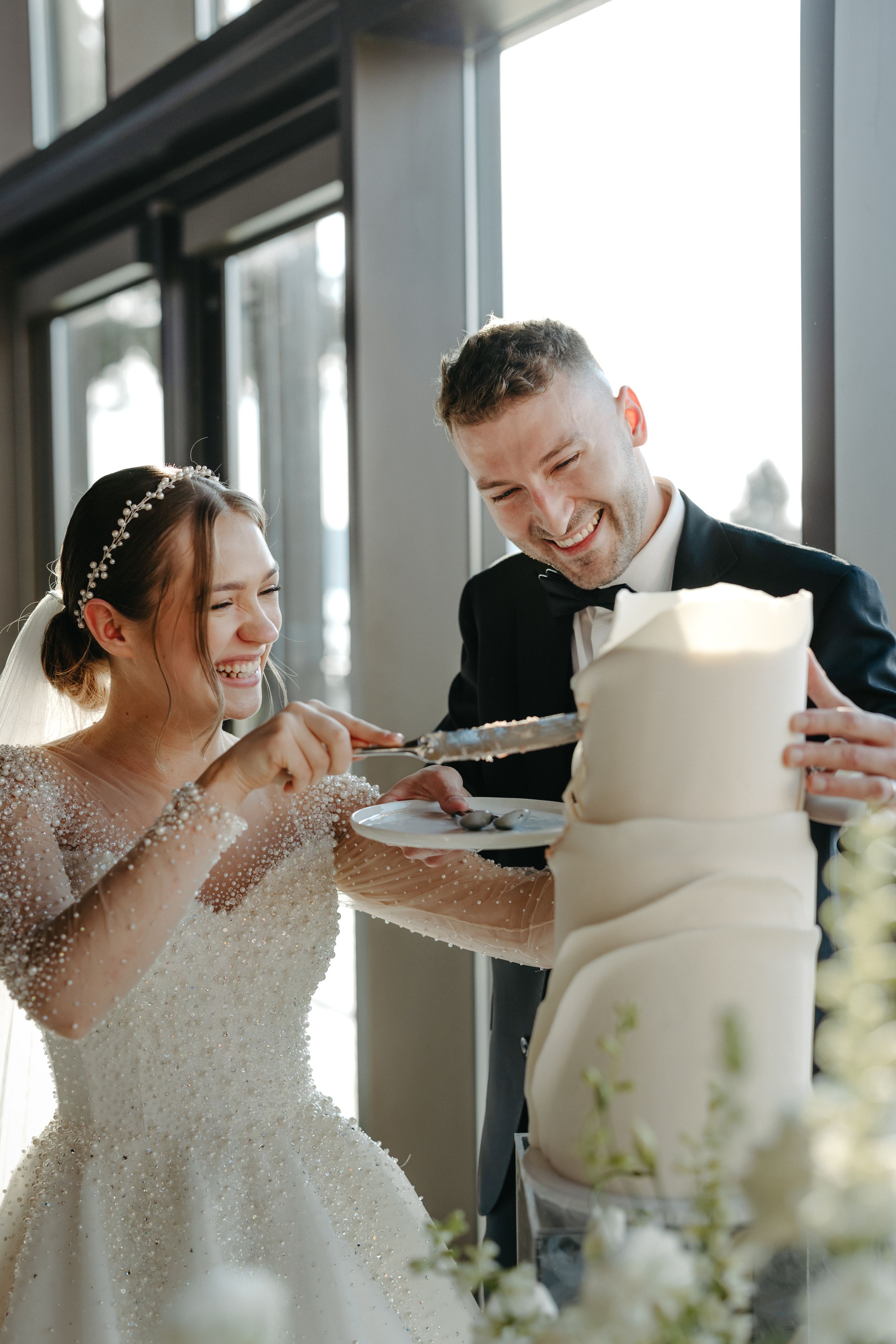 Wedding cake cutting moment in front of large windows with natural light.