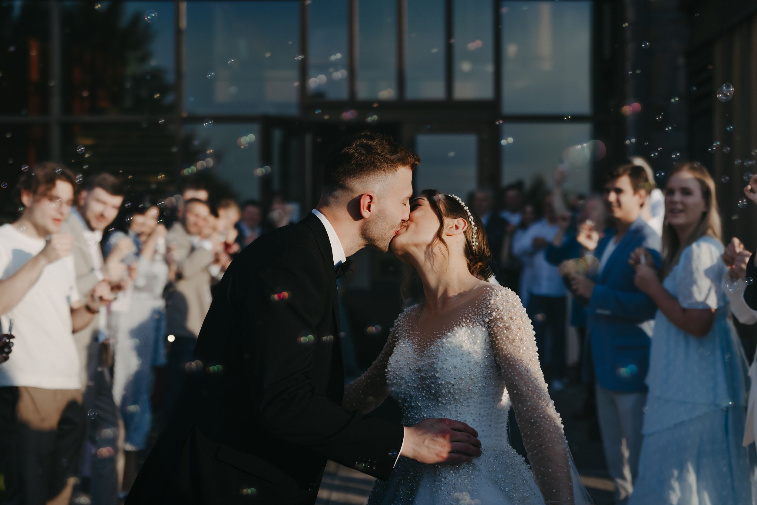 A couple shares a romantic embrace at their wedding celebration surrounded by guests with sparklers.