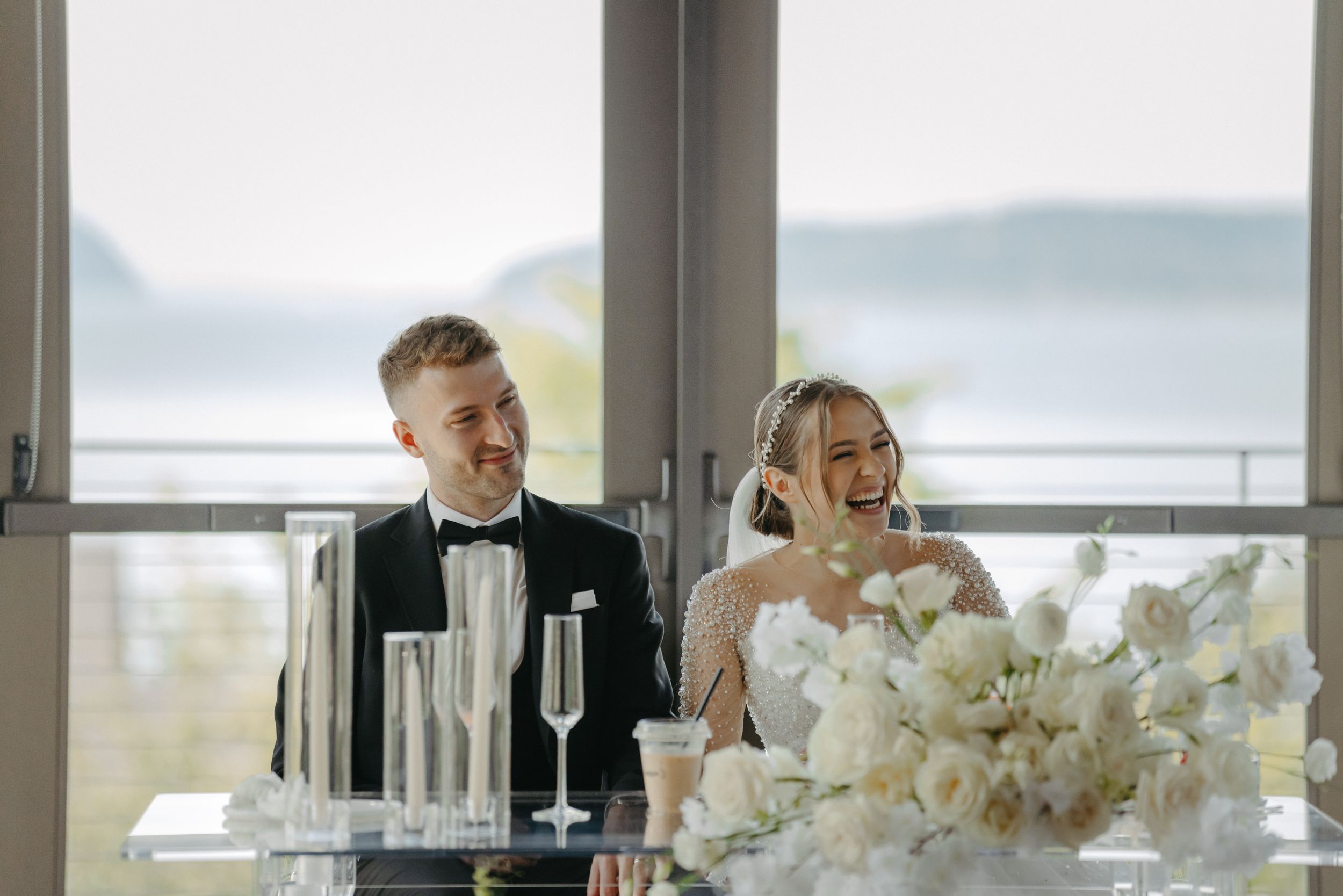 An elegant wedding reception setup with white floral arrangements and waterfront views.